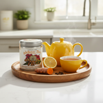 Turmeric Ginger Citrus Herbal Tisane tin with yellow ceramic teapot and cup on wooden tray with turmeric root and lemon