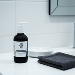 Activated Charcoal & Willow Bark Cleanser on clean white bathroom counter with charcoal grey towel, minimal shelfie