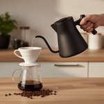 Fellow Corvo EKG Pro matte black electric kettle mid-pour over ceramic pour over dripper on wood surface with coffee beans