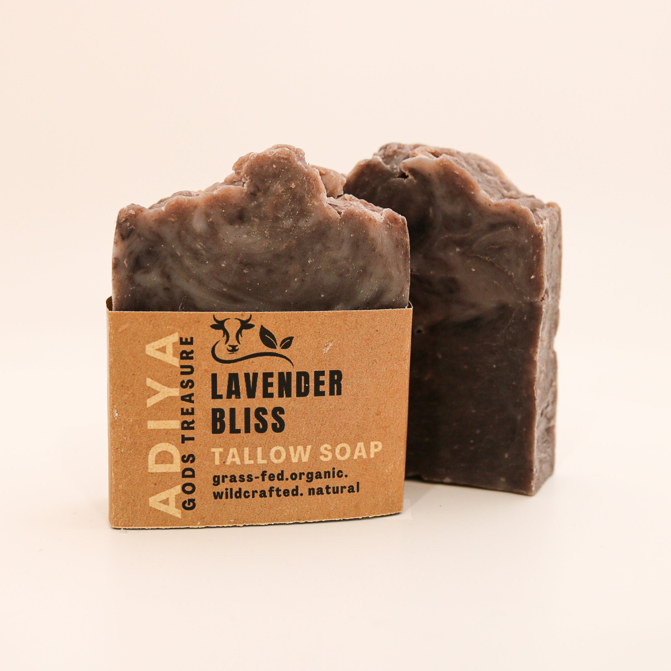 Two bars of "lavender bliss" tallow soap next to its cardboard box on a beige background