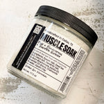 A clear plastic jar with a black lid labeled 'MUSCLE SOAK', indicating it is a bath additive for sore muscles.