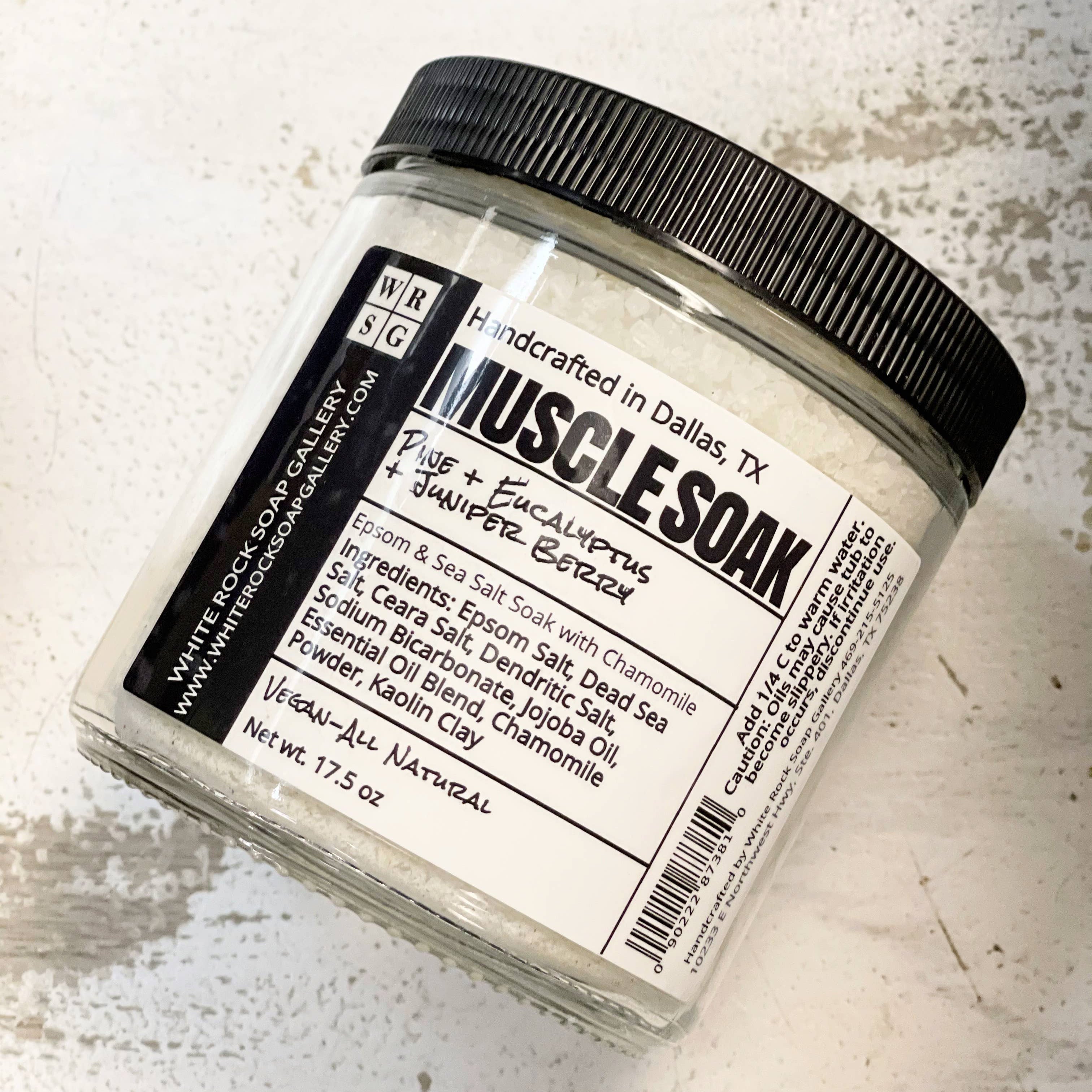 A clear plastic jar with a black lid labeled 'MUSCLE SOAK', indicating it is a bath additive for sore muscles.