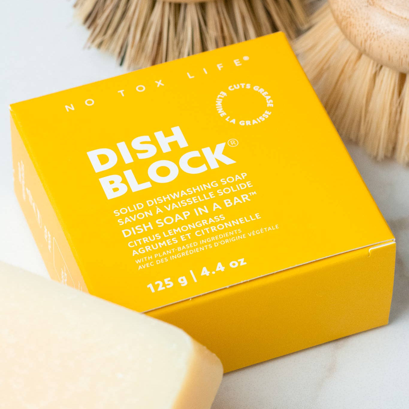 Yellow box of Dish Block soap with a bar of soap and brushes on a white surface