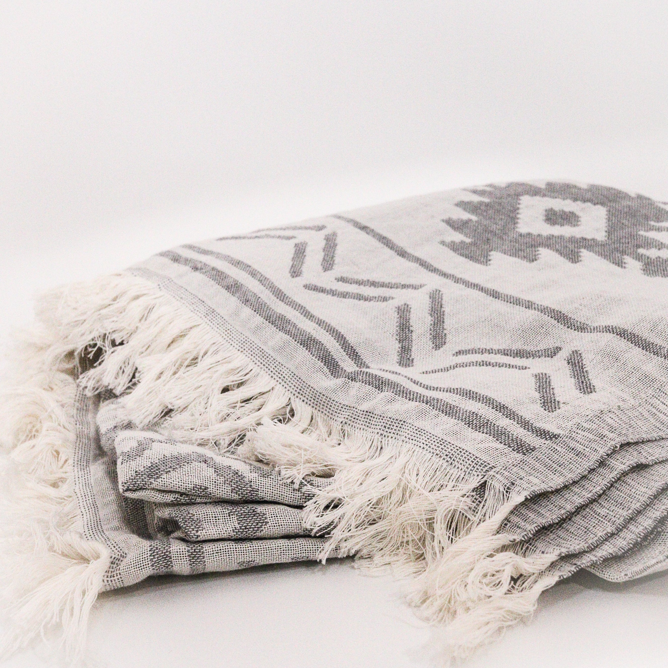 Aztec pattern grey and white patterned Turkish towel with fringes on a light background