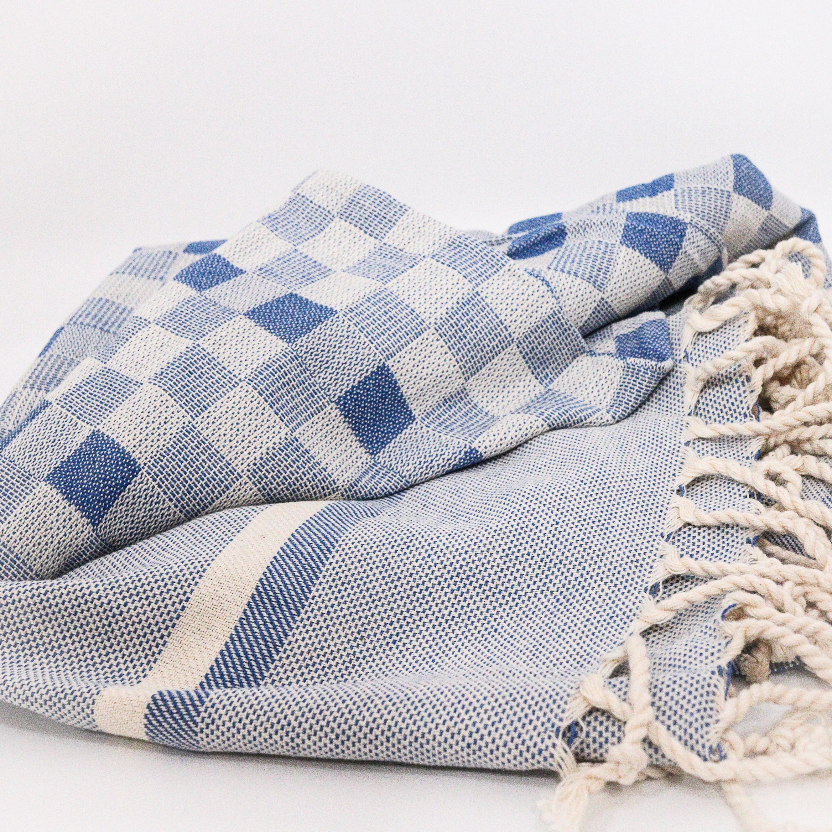 Blue and white checkered organic cotton Turkish towel with tassels on a light gray background